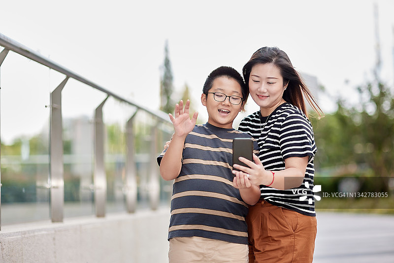 微笑的东亚母子在户外用手机与亲戚视频通话图片素材