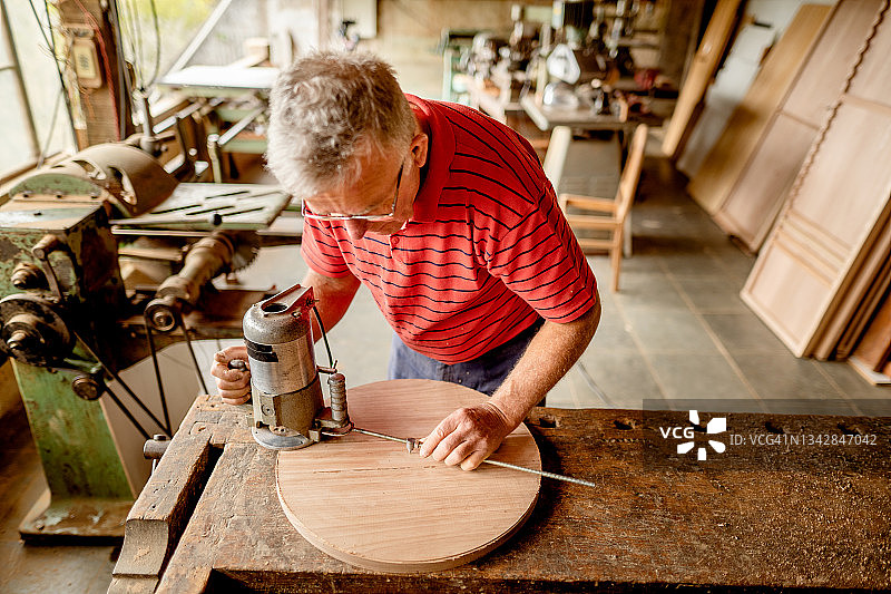 年长的男人在他的木工车间使用路由器来塑造木材图片素材