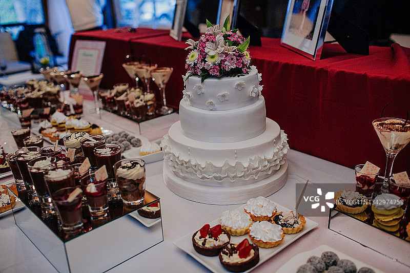 多种甜点台上，顶部饰有彩色天然鲜花的白色婚礼蛋糕图片素材