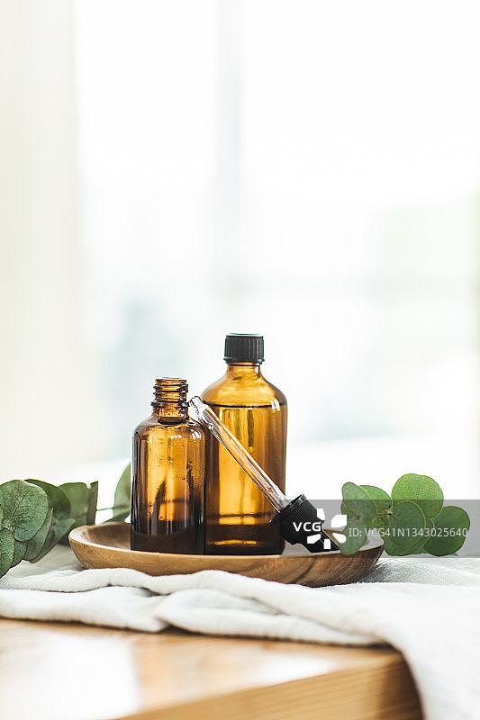 带有桉树叶的木板上装有化妆油的棕色琥珀玻璃瓶滴管图片素材