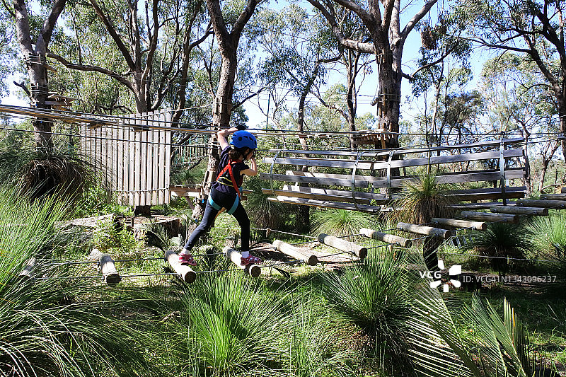 年轻的澳大利亚女孩穿过木桥攀爬绳索图片素材
