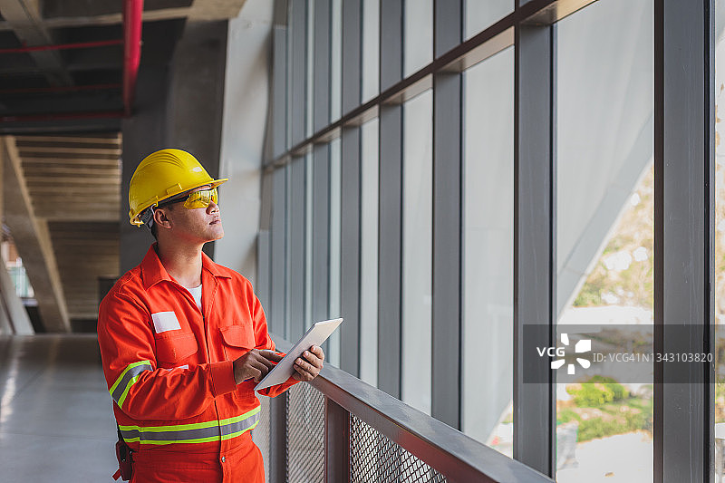 在建筑工地窗边使用平板电脑的亚洲建筑或电子工程师肖像图片素材
