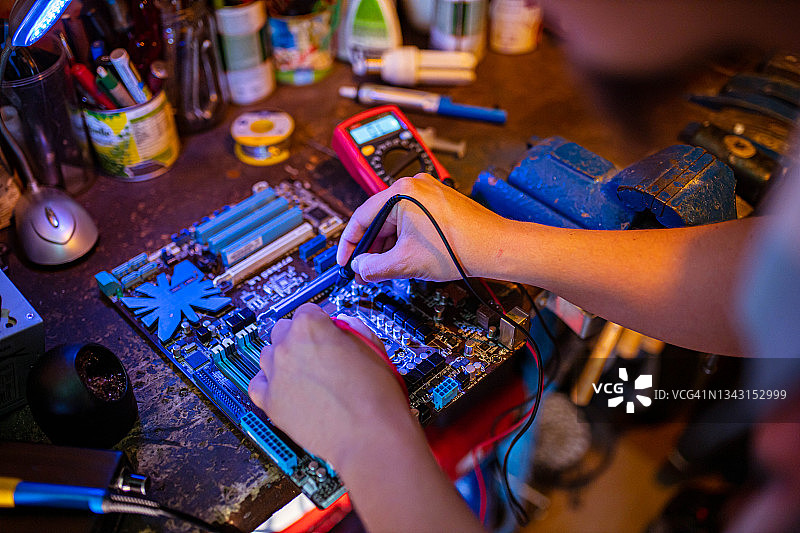 维修工程师在他的工作室里使用万用表测量主板的电气活动图片素材