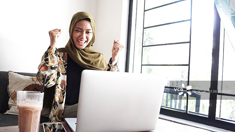 兴奋的亚洲穆斯林年轻女人在使用笔记本电脑图片素材