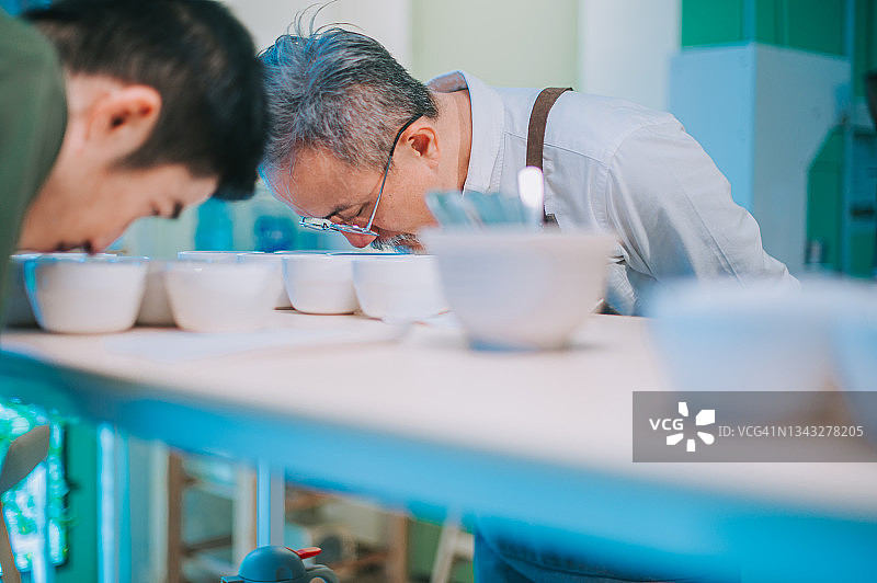专业亚裔咖啡师进行咖啡杯测，弯腰仔细闻咖啡图片素材