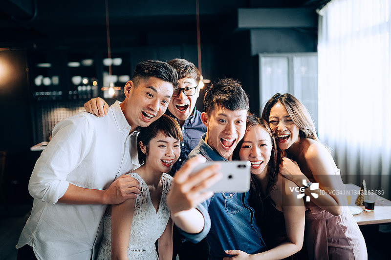一群快乐的亚洲年轻男女在聚会上用智能手机自拍图片素材
