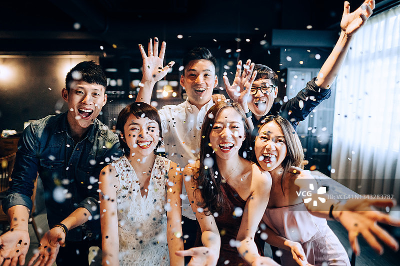 一群快乐的亚洲男人和女人在聚会上玩耍并吹着闪闪发光的彩纸图片素材