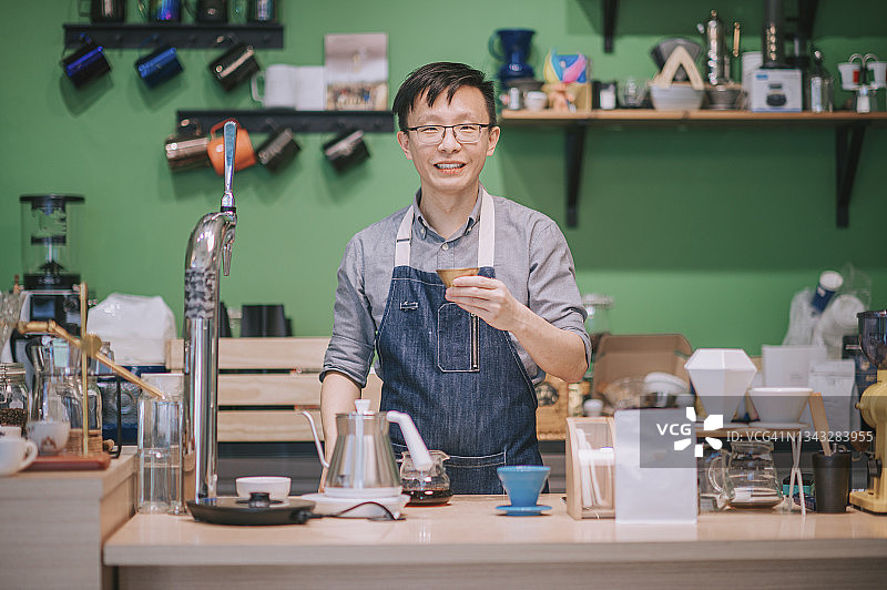 在咖啡馆吧台看着镜头微笑的亚洲华人咖啡师肖像图片素材