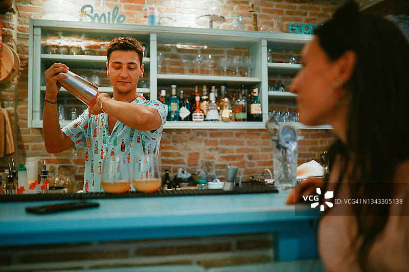 年轻调酒师调制鸡尾酒并与女士交谈图片素材