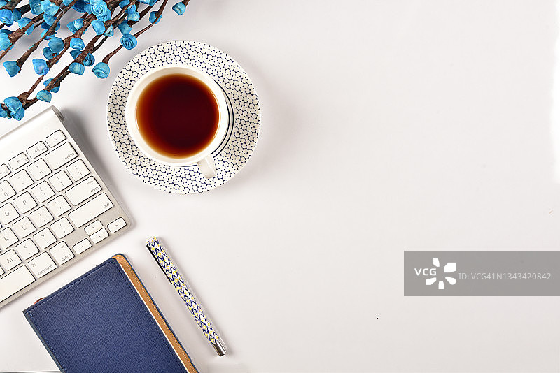 办公桌俯视图，配有电脑键盘、茶杯和蓝色鲜花图片素材