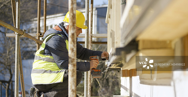 男性建筑工人在房屋外墙上钻孔图片素材