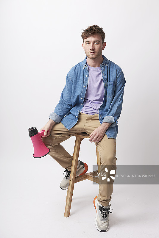 年轻人沮丧地坐在凳子上，身旁放着一个扩音器图片素材