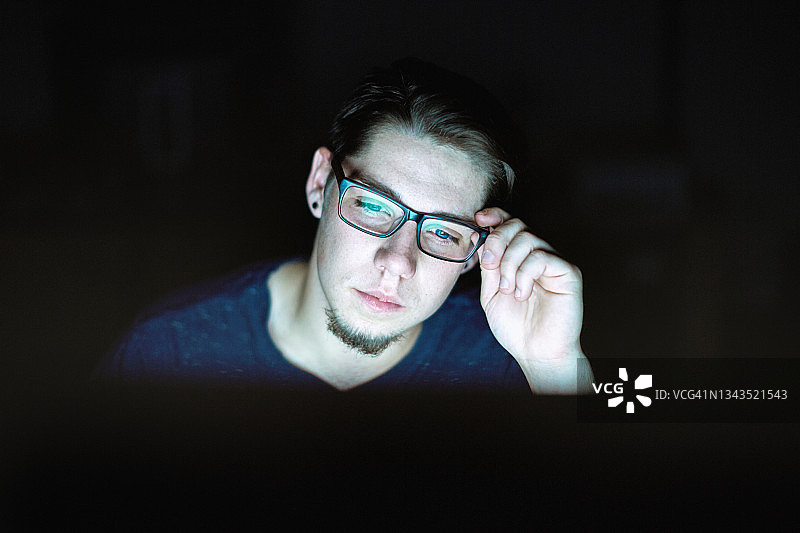 年轻男人坐在电脑前，调整眼镜，熬夜工作，很疲惫图片素材