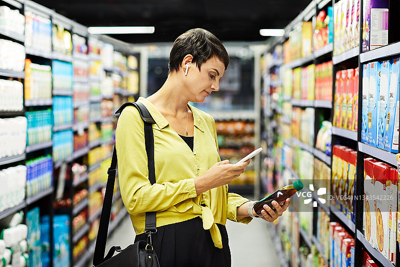 年轻女子在超市浏览商品时使用手机照片图片素材