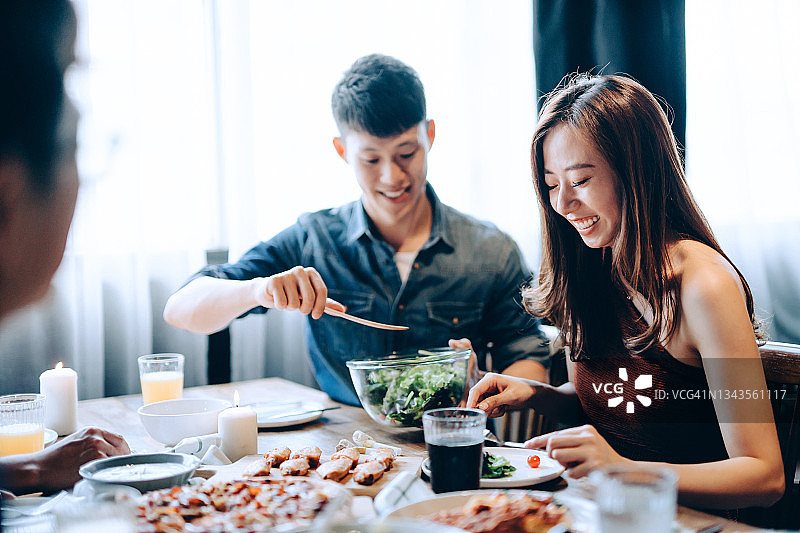 快乐的年轻亚洲男人与一群朋友分享食物。他们在晚宴上玩得开心，聊天和享用美食和饮料图片素材
