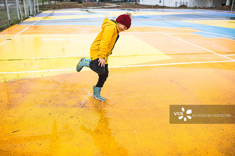 可爱的男孩单腿跳跃在水坑里玩耍图片素材