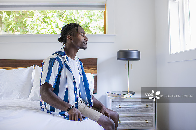 坐在床上看着窗外的年轻男人图片素材