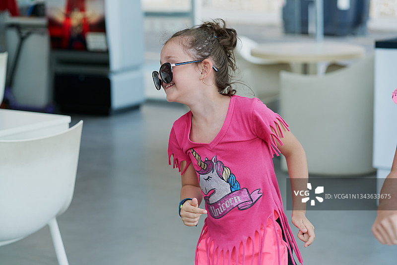 快乐的女孩戴着太阳镜，身穿粉色衣服在开放空间行走图片素材