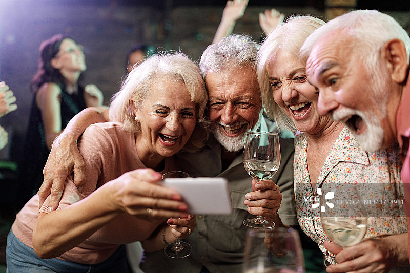 快乐的老年朋友在酒吧夜出时使用手机图片素材