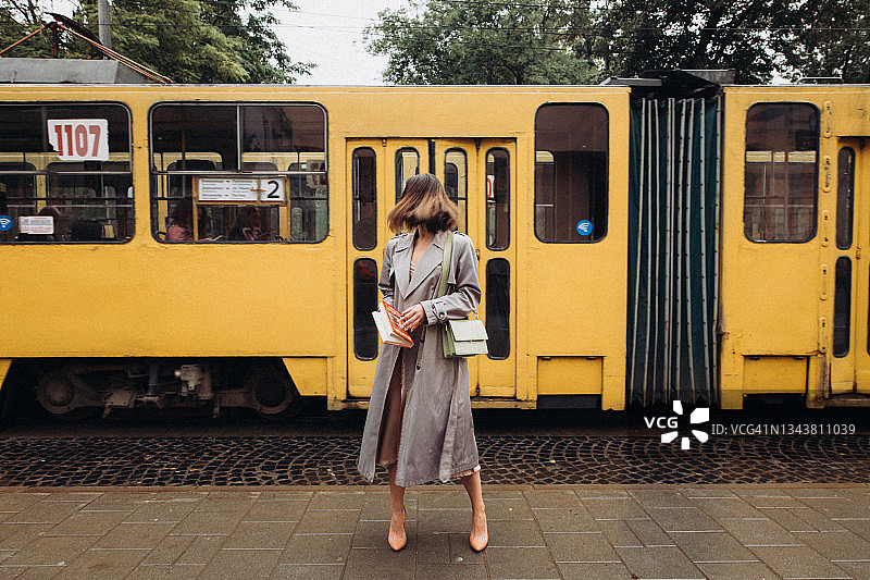 穿着风衣的美丽女人站在电车背景前图片素材
