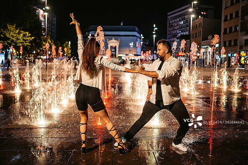 在彩色喷泉旁跳舞的年轻情侣图片素材