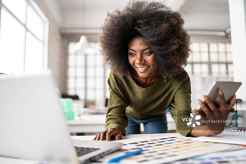 在创意办公室里，笑容满面的非洲裔女设计师正在使用笔记本电脑工作图片素材