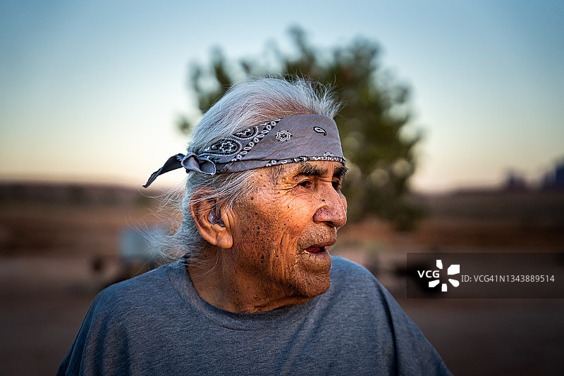 在犹他州或亚利桑那州纪念碑谷的后院里，在阳光明媚的午后对着镜头微笑的年长纳瓦霍美国原住民男人肖像图片素材