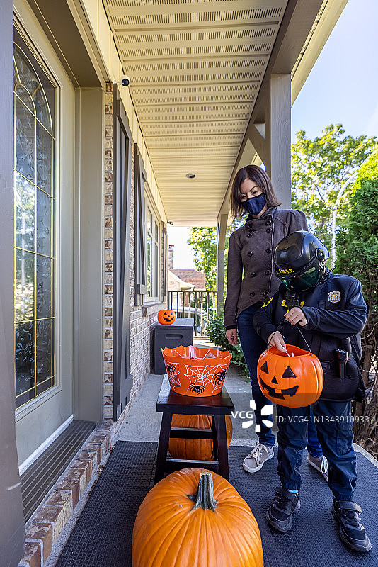 万圣节戴着防护口罩、穿着警官服装拿糖果的男孩图片素材