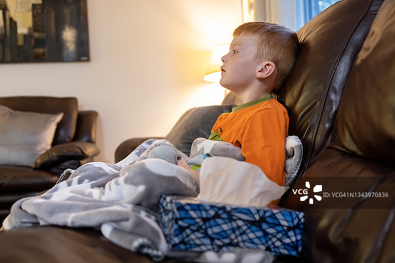 红发小男孩生病在家坐在沙发上图片素材