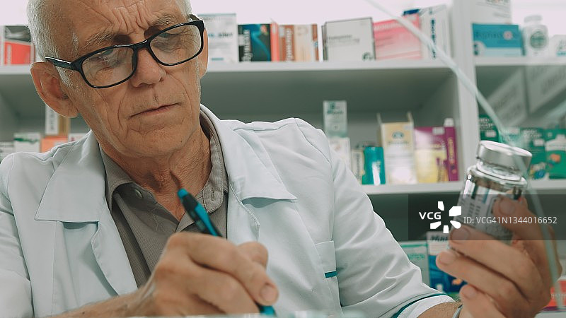 药剂师在药房拿着药罐，阅读成分并记录图片素材