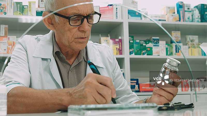 药房里的男药剂师拿着药罐，阅读其成分并在文件夹中书写图片素材
