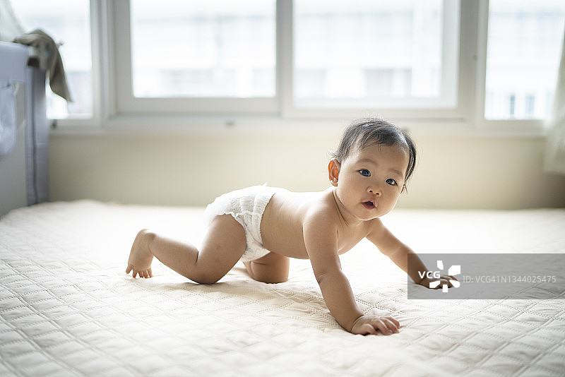 亚洲婴儿穿着尿布在舒适的床上尝试爬行，母亲在前面鼓励图片素材