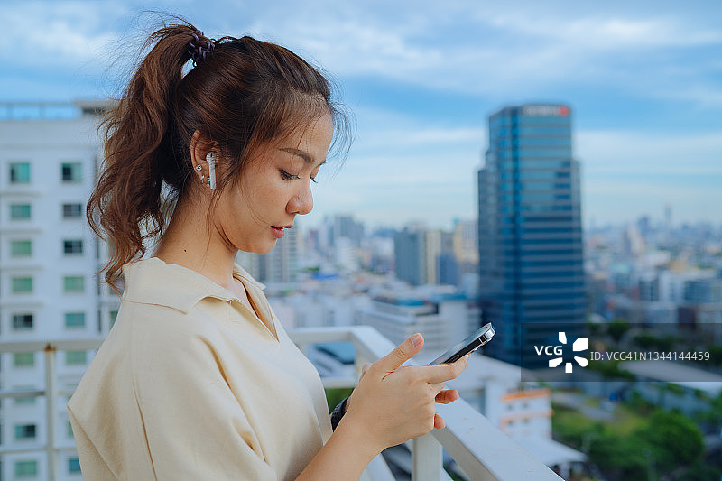 戴着Airpods用智能手机在线听音乐的亚洲女孩图片素材