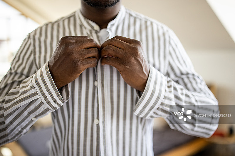 年轻男子早上在卧室里穿好衣服并扣上衬衫图片素材