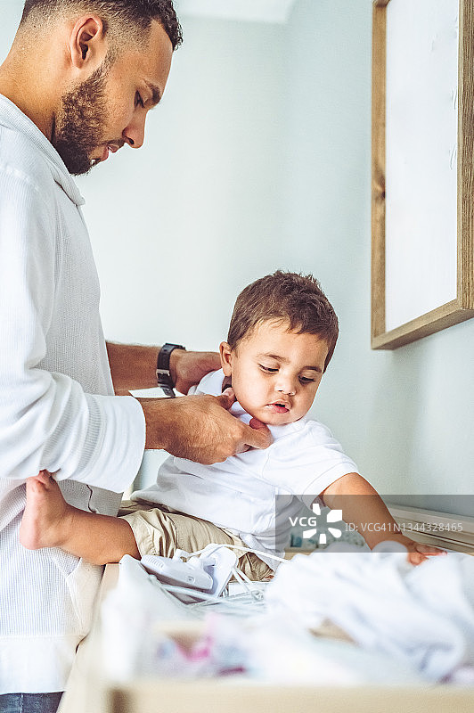 多种族父亲为幼儿穿衣服，童年和育儿图片素材