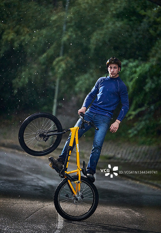 在一个下雨的夏日午后，年轻的成年人在黄色越野自行车上保持平衡图片素材