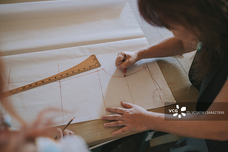 亚裔女裁缝指导学生在纸上绘制时装设计稿特写图片素材