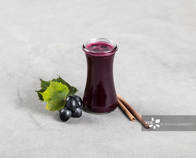 浅灰色背景下的玻璃瓶装黑葡萄饮品与竹吸管图片素材