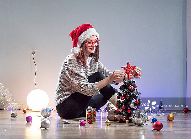 快乐的女人装饰她的圣诞树，并将星星放在顶部图片素材