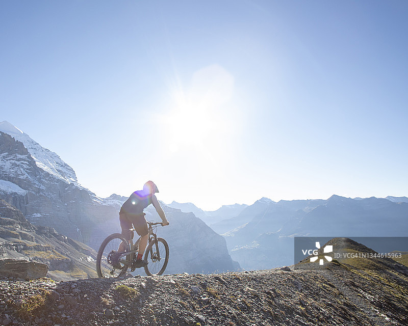 年轻男子在阳光明媚的山脊上骑山地自行车图片素材