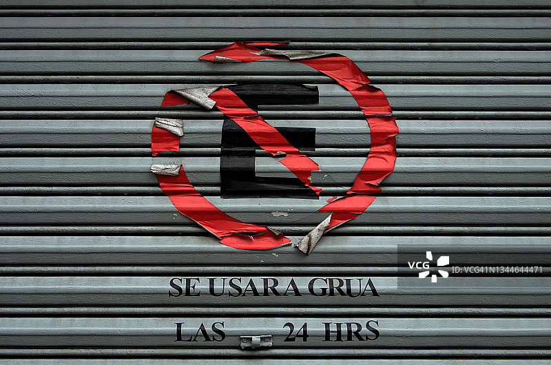 建筑卷帘门上贴着的西班牙语贴纸，上面写着“禁止停车，24小时使用拖车”图片素材