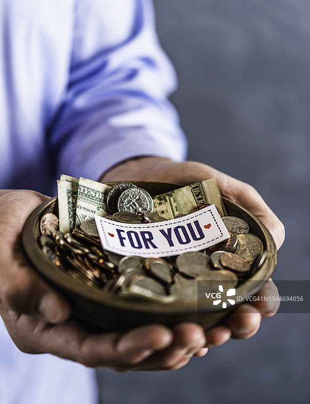 手捧装满硬币的捐款碗的身份不明的男人图片素材