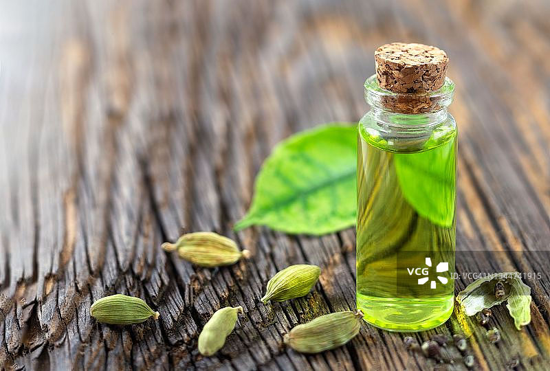 木制背景上的小豆蔻精油瓶与小豆蔻籽和叶子图片素材