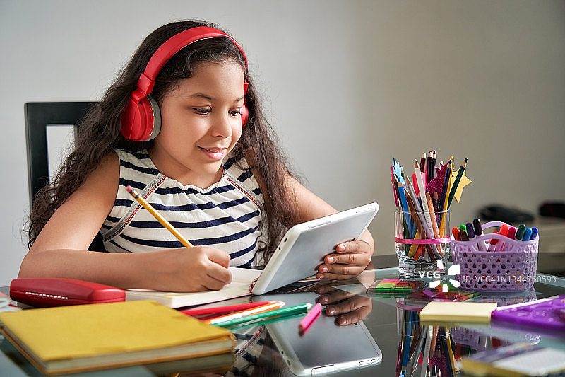 戴着耳机、用平板电脑在家上网课的小女孩图片素材
