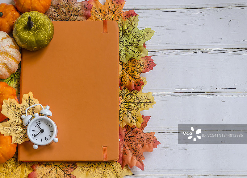 秋叶，南瓜，复古闹钟和橙色记事本装饰木桌，顶部视图和复制空间图片素材