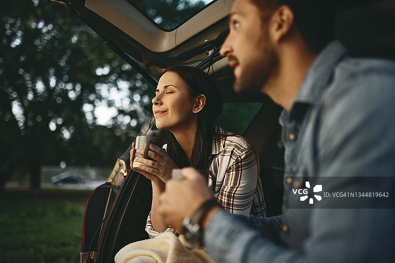 日落时分坐在车里喝咖啡的年轻情侣图片素材