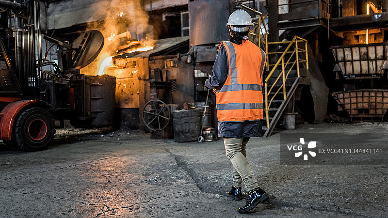 身穿橙色反光背心的工人在铸造厂的工业场景中行走图片素材