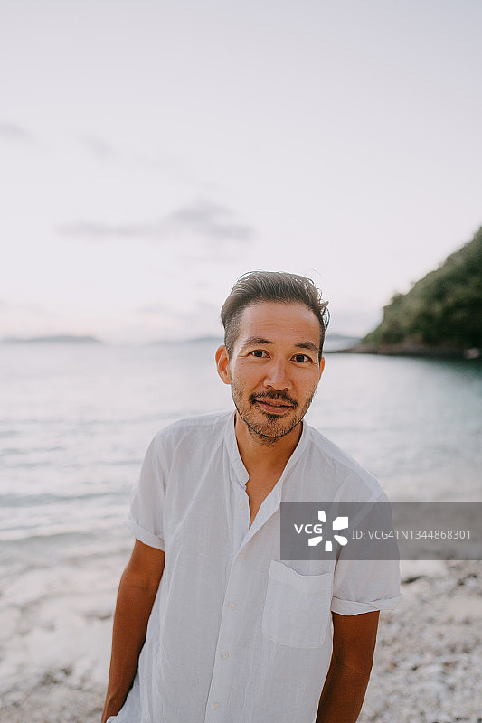日落时分在海滩上看镜头的日本男人图片素材