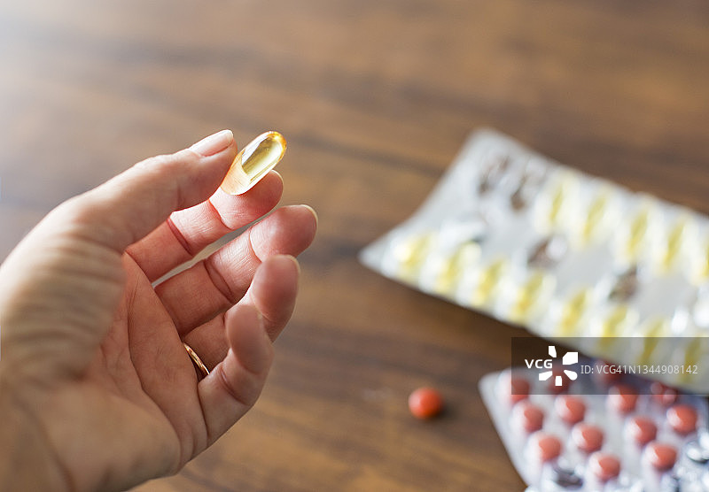 特写：女人手拿黄色Omega-3营养补充剂胶囊图片素材