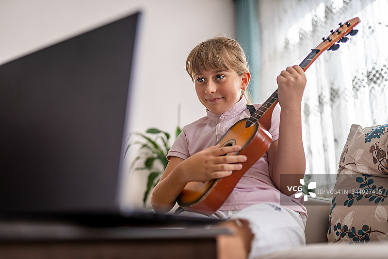 小女孩在线学习吉他课程，对着笔记本电脑弹吉他图片素材